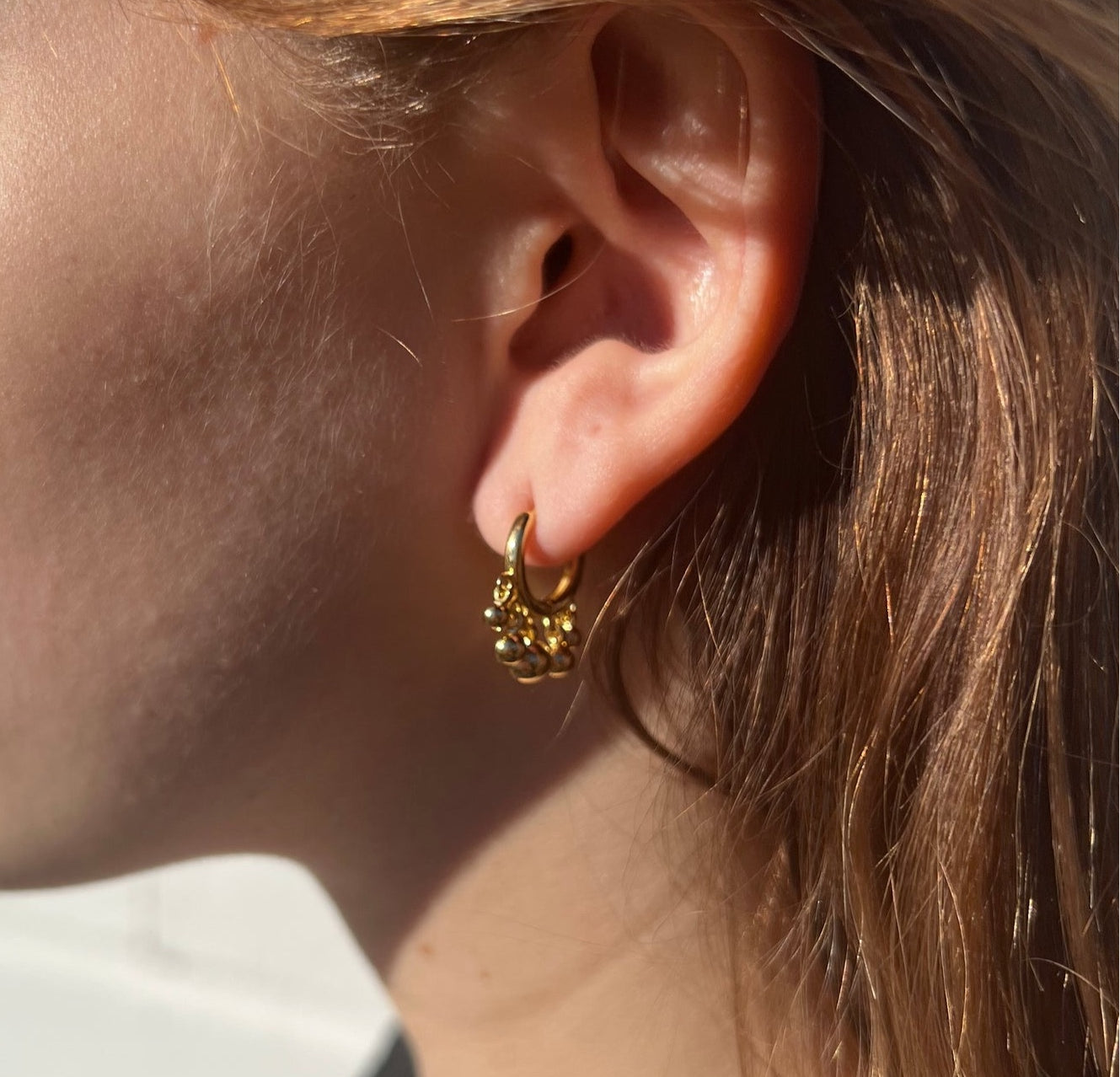 Small gold hoop with tasseled gold beads in ear.