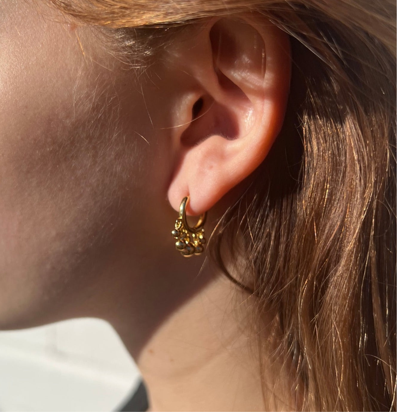 Small gold hoop with tasseled gold beads in ear.
